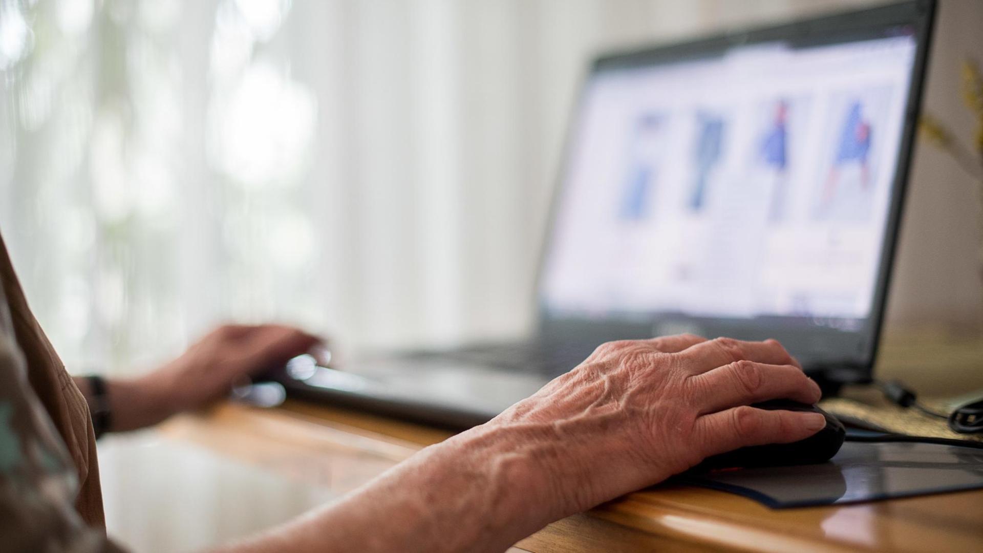 Eine Seniorin sitzt an ihrem Laptop und hat ihre Hand auf einer Maus liegen