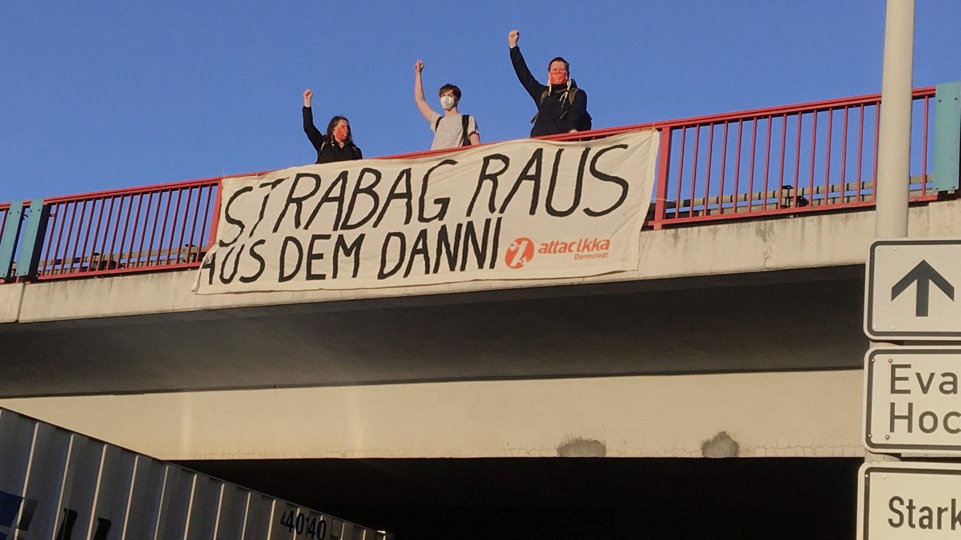 Auf einer Autobahnbrücke posieren drei Aktivisten vor einem Stofftransparent mit der Aufschrift "Strabag raus aus dem Danni"