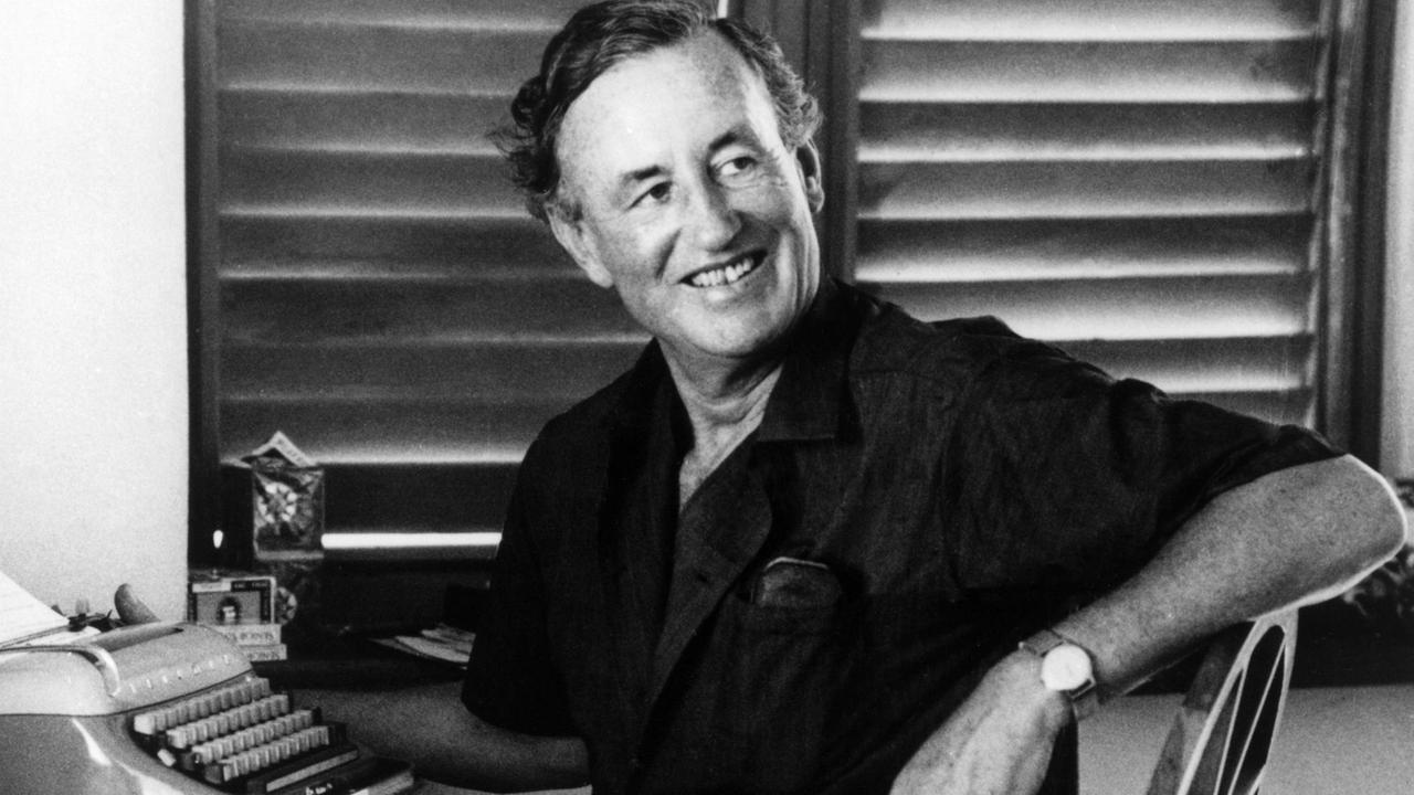 Der britische Autor Ian Fleming sitzt lächelnd an seiner Schreibmaschine