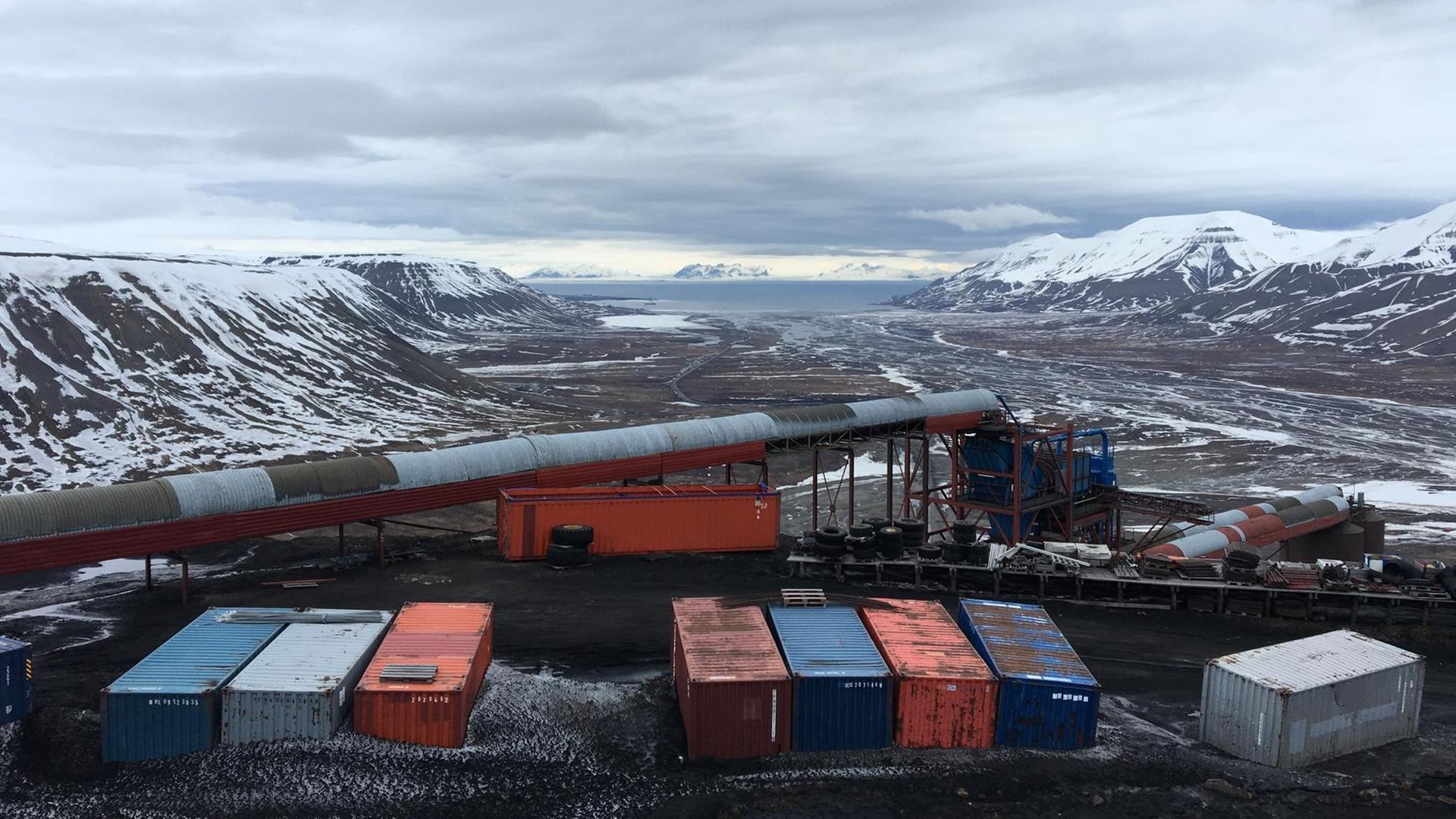 Ausblick in eine Kohlegrube mit bunten Containern, im Hintergrund erstreckt sich eine winterliche Berglandschaft