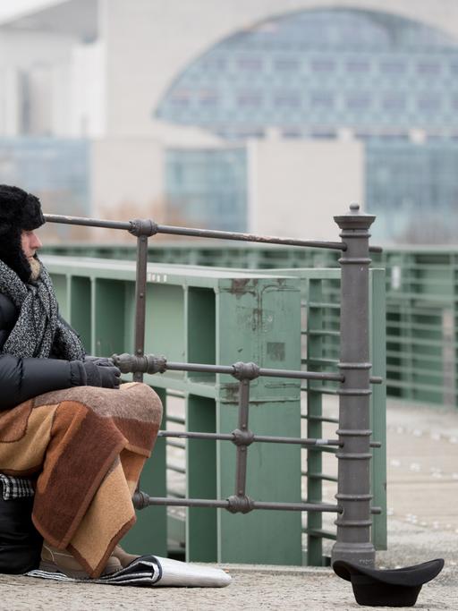 Udo, ein Obdachloser, sitzt in Berlin an der Spree im Regierungsviertel und bittet um Unterstützung.