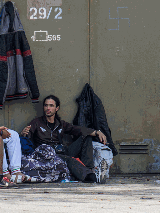 Mehrere Flüchtlinge sitzen am 10.10.2014 in München (Bayern) auf dem Gelände der Bayernkaserne neben ihren Koffern auf dem Asphalt. Am Abend zuvor haben rund 150 Flüchtlinge für eine bessere Unterbringung demonstriert.