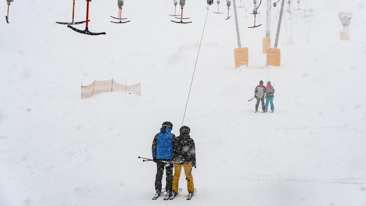 Bayern, Sankt Englmar: Wintersportler fahren am Predigtstuhl mit einem Skilift im Schneegestöber. 