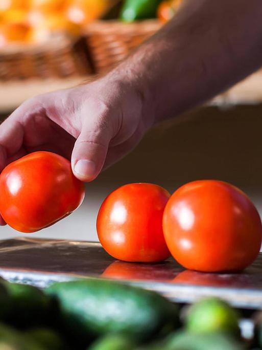 Eine Person legt in einem Supermarkt Tomaten auf eine Waage.
