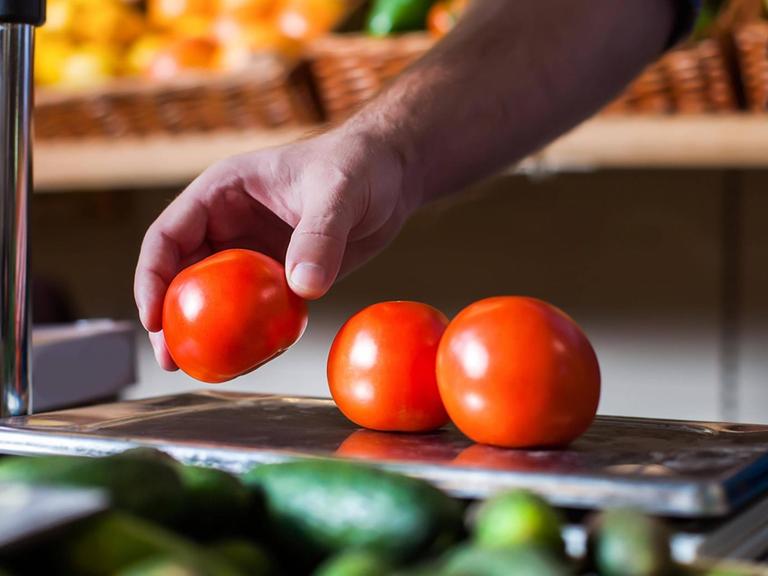 Eine Person legt in einem Supermarkt Tomaten auf eine Waage.