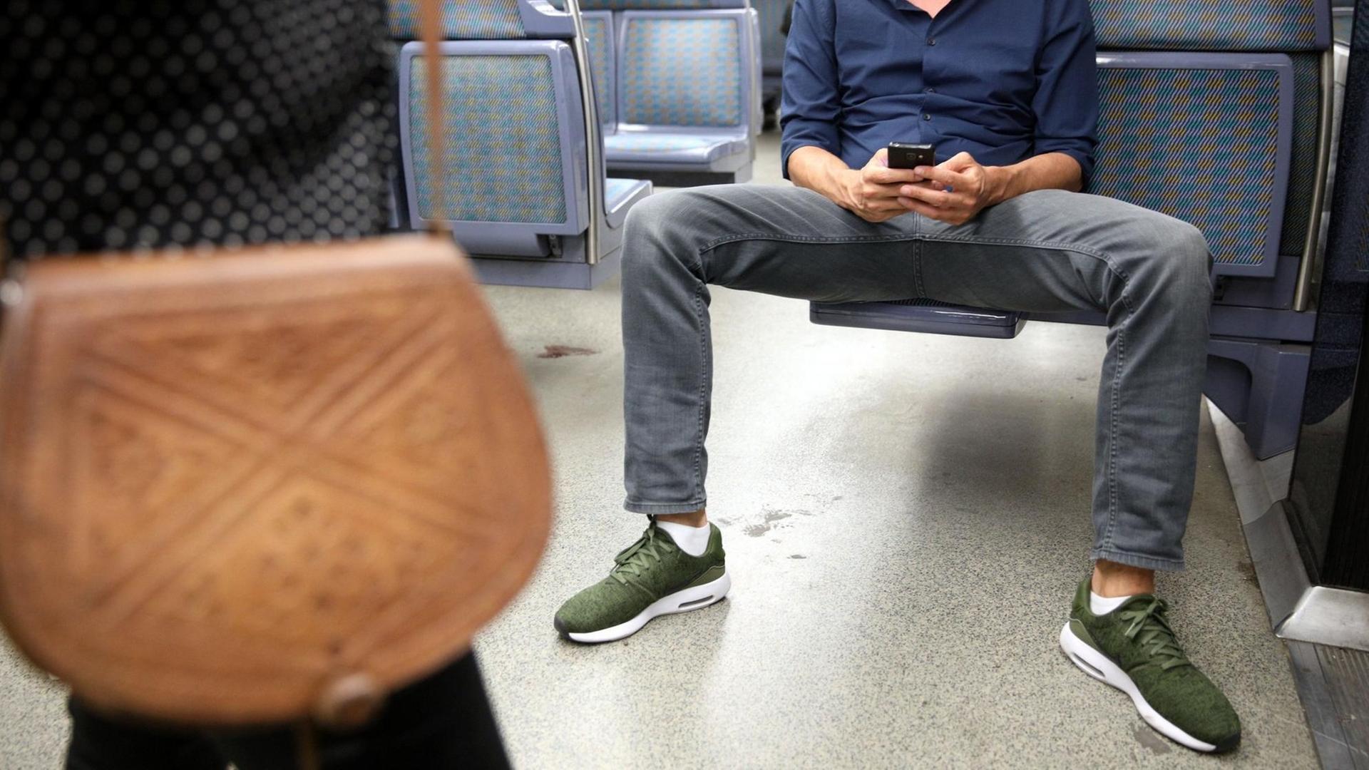 Ein Mann sitzt in der U-Bahn breitbeinig auf einem Sitz und versperrt so den Platz für andere Fahrgäste. 