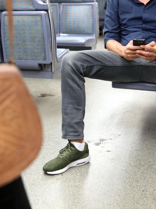 Ein Mann sitzt in der U-Bahn breitbeinig auf einem Sitz und versperrt so den Platz für andere Fahrgäste. 