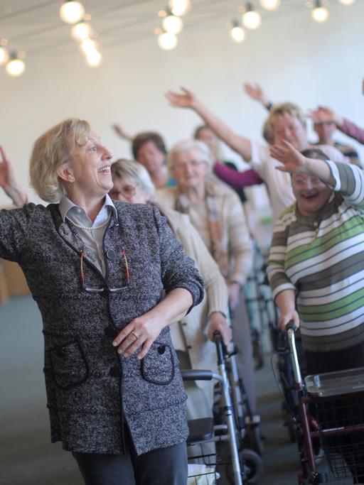 Eine Dame unterrichtet in einem Altenheim eine Gruppe Senioren beim Tanzen.