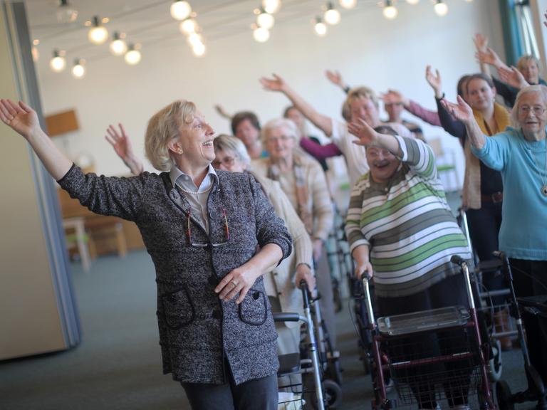 Eine Dame unterrichtet in einem Altenheim eine Gruppe Senioren beim Tanzen.