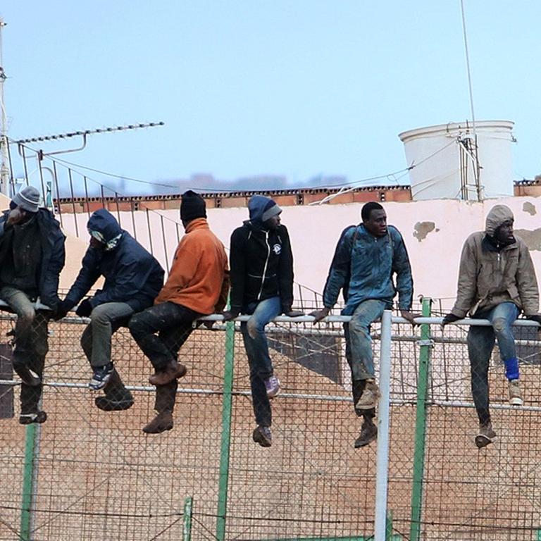Migranten sitzen auf dem Grenzzaun zwischen Marokko und Spanien in Melilla.
