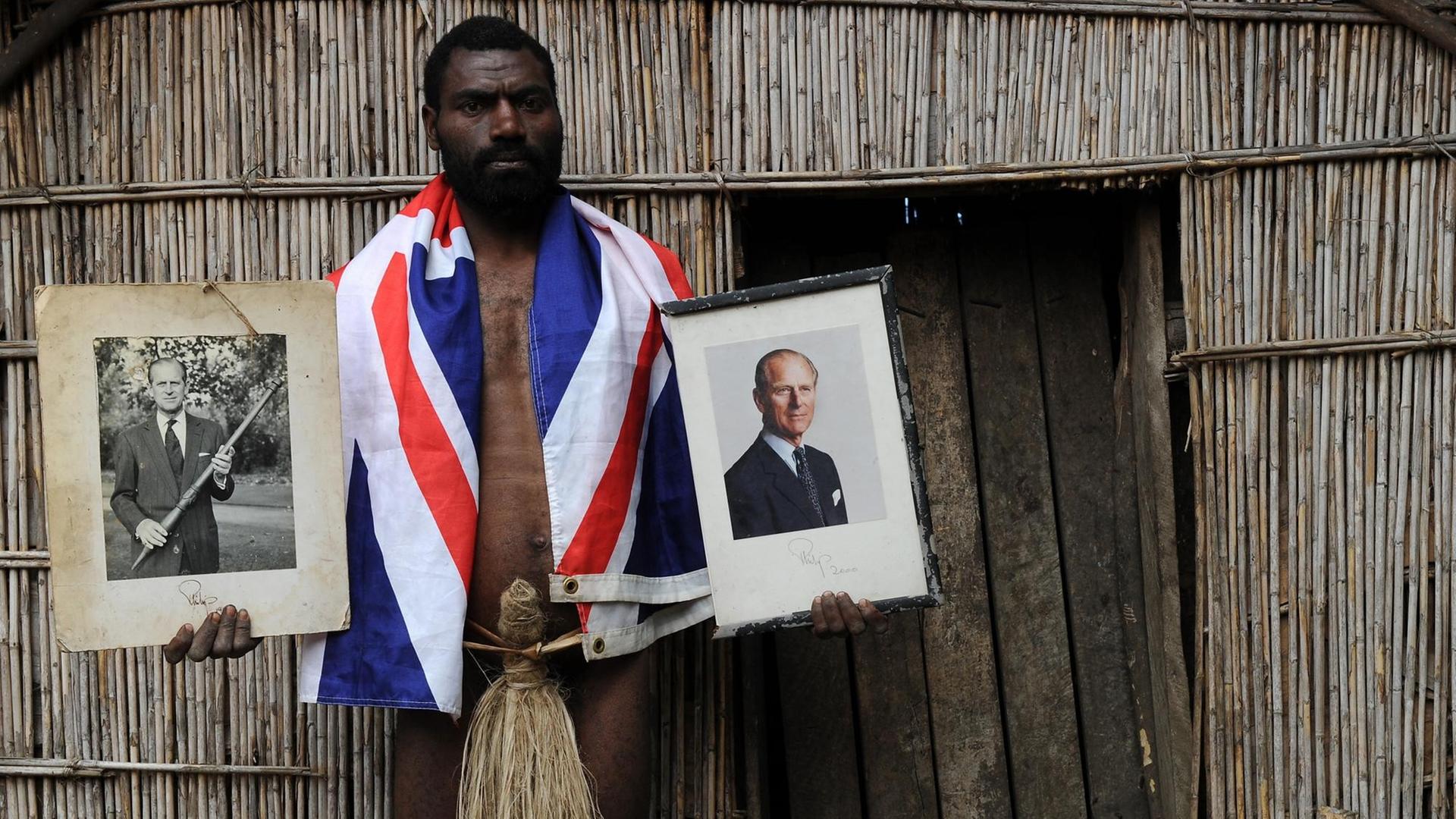 Chief Siko hält zwei Bilder seiner Gottheit Prince Philip in Händen. Bekleidet ist er mit einem Penisköcher und einem Union Jack. (Bild: Torsten Blackwood / AFP)