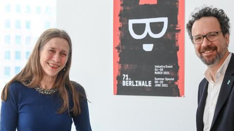 Das Leitungs-Duo der Berlinale, Mariette Rissenbeek, Geschäftsführerin, und Carlo Chatrian, künstlerischer Direktor, stehen im Berlinale-Büro am Potsdamer Platz. Im Hintergrund ein Poster des Festivals.