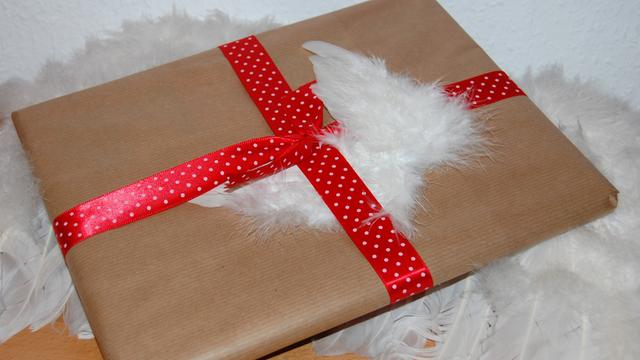 Buch, das in einfachem Packpapier verpackt ist, mit Engelsflügel als Deko (Aufnahme in Dortmund, 14. November 2010).
