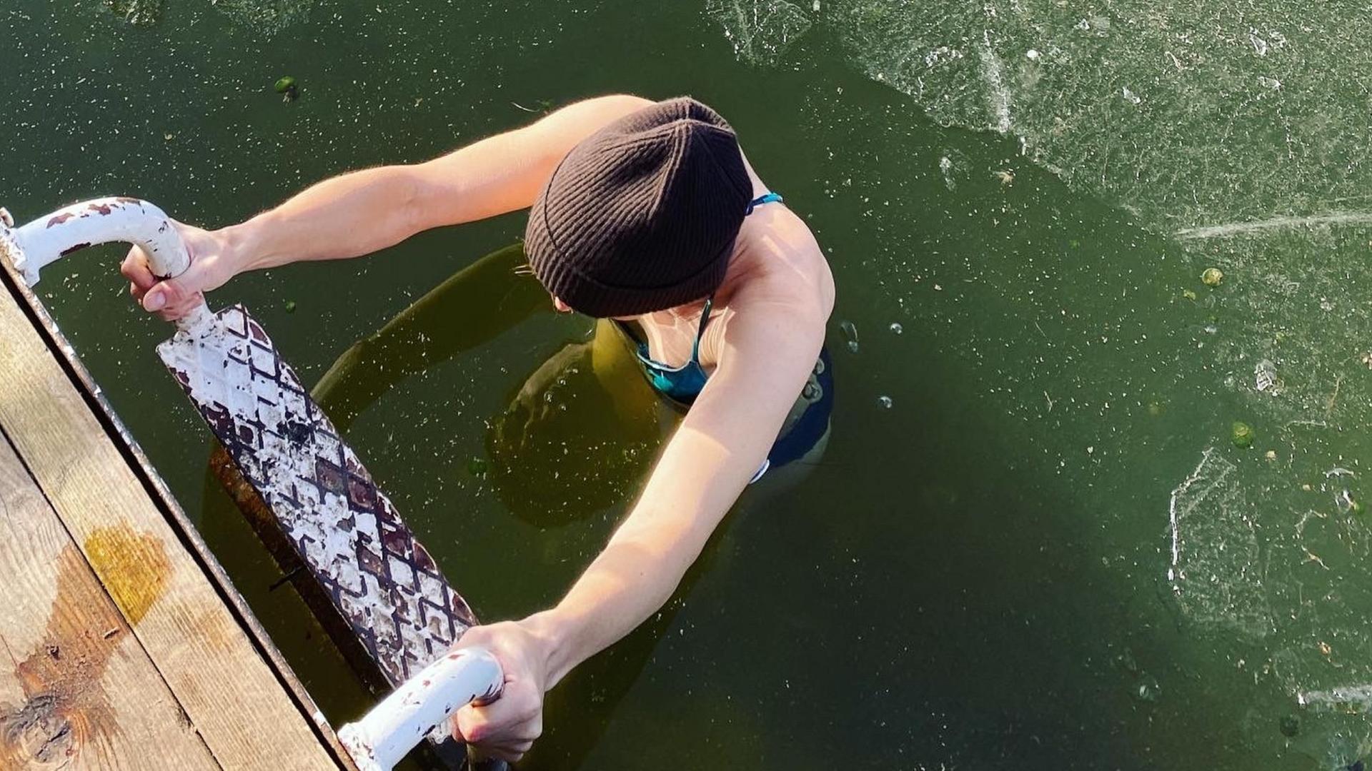 Eine Frau beim Eisbaden im See; nach dem Bad steigt sie die Leiter hoch, auf dem Wasser ist eine dünne Eisschicht zu sehen.