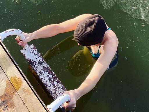 Eine Frau beim Eisbaden im See; nach dem Bad steigt sie die Leiter hoch, auf dem Wasser ist eine dünne Eisschicht zu sehen.