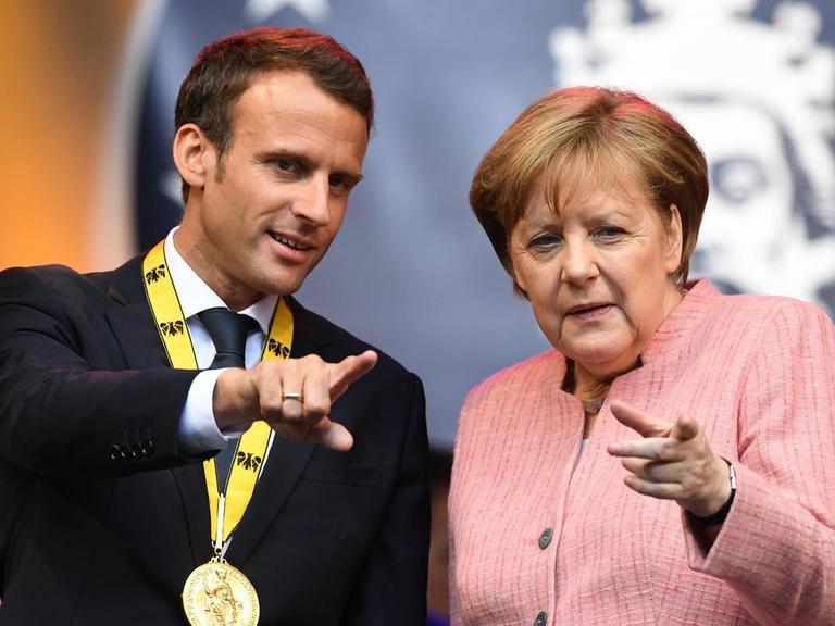 Bundeskanzlerin Angela Merkel (CDU), und der französische Staatspräsident Emmanuel Macron stehen nach der Verleihung des Karlspreises auf einer Tribüne.