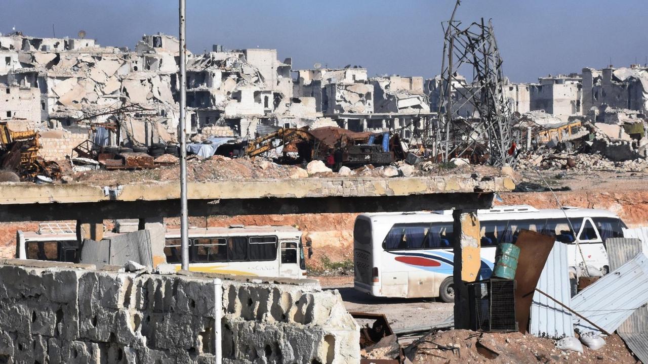 Busse vor dem zerstörten Ostteil der syrischen Stadt Aleppo