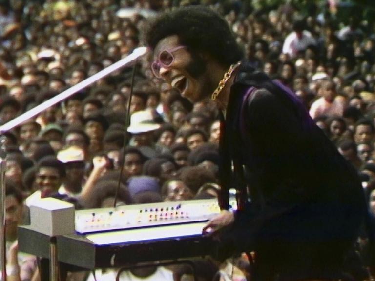 Sly Stone performt auf dem Harlem Cultural Festival, im Hintergrund ist das Publikum zu sehen.