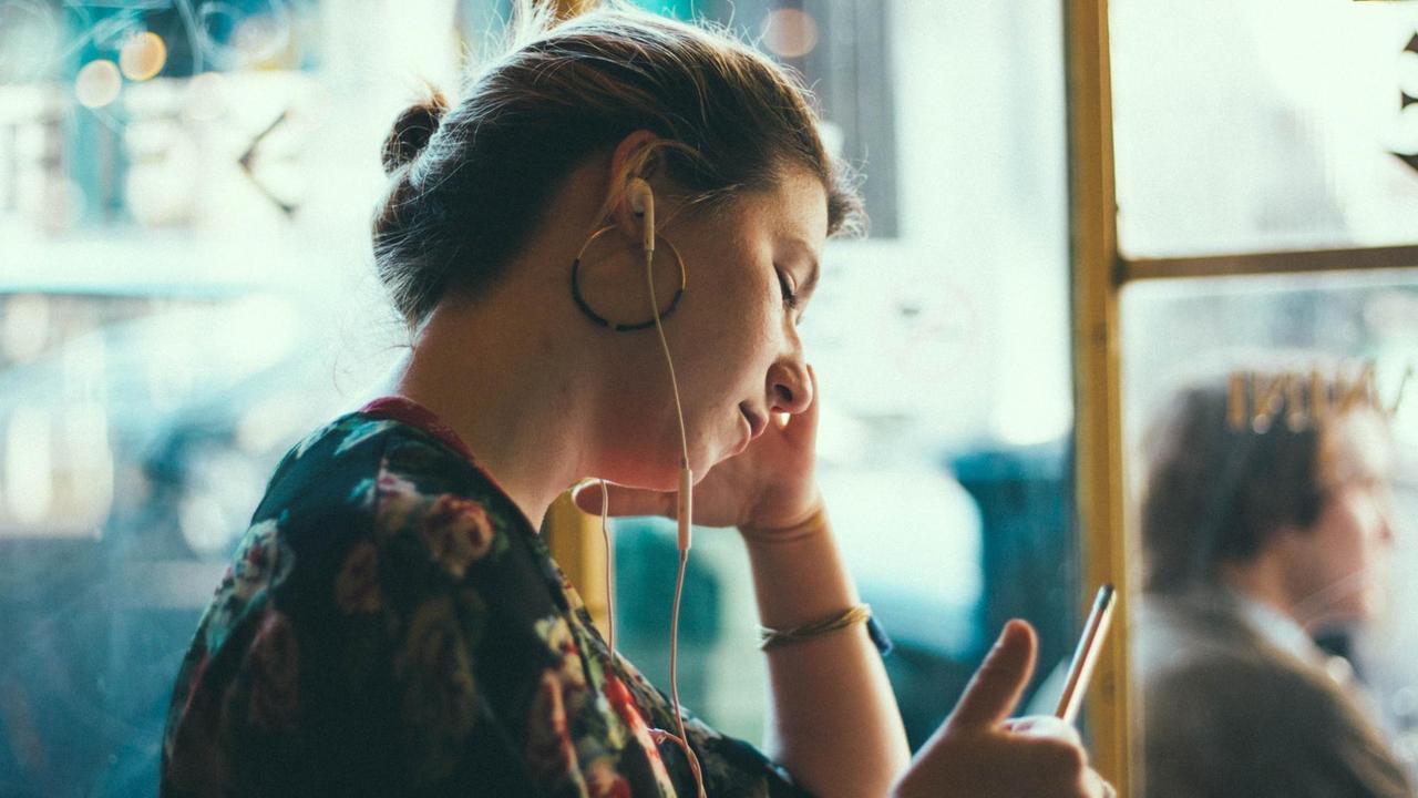 Eine junge Frau hört mit Kopfhörern Audios über ihr Handy.