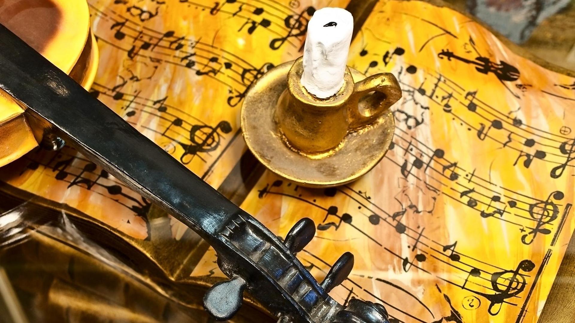 Eine unspielbare Geige mit fehlenden Saiten ruht auf einem nachgemachten Notenheft, das voller falscher, unspielbarer Notenzeichen ist. Auf den Seiten steht ein Kerzenständer, der wie eine Kulisse aus Knete aussieht.