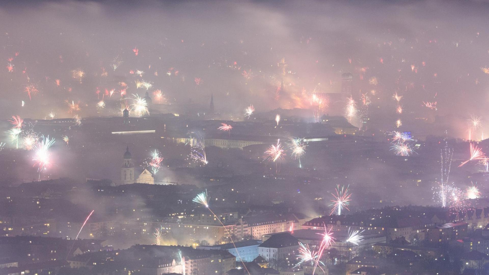 Feuerwerksraketen explodieren in der Silvesternacht über München und hüllen die Innenstadt in dichten Rauch.