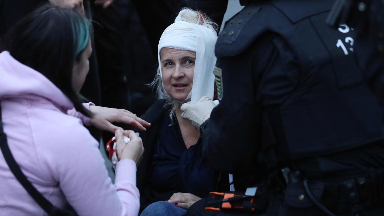 Eine verletzte Frau auf einer rechten Demonstration in Chemnitz wird am blutenden Kopf von einem Polizisten verbunden.