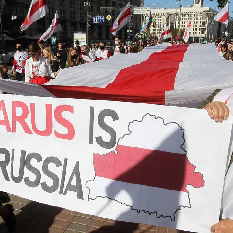Protestanten halten die rot-weiße Flagge von Belarus während einer Demonstration in Kiew, auf einem Plakat steht: "Belarus is nor Russia"