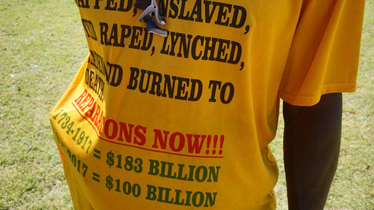 Ein Mann hält sein gelbes T-Shirt in die Kamera, auf dem die genauen Summen für Reparationszahlungen stehen.