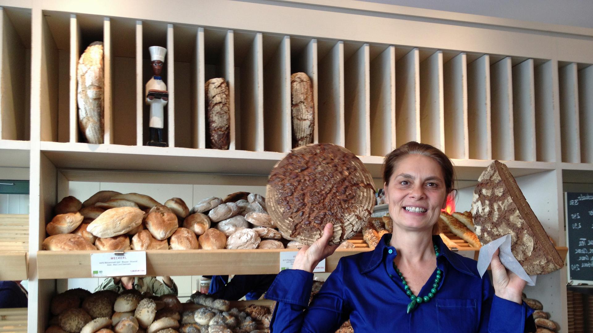 Sarah Wiener steht vor einem Regal hält Brot in den Händen.
