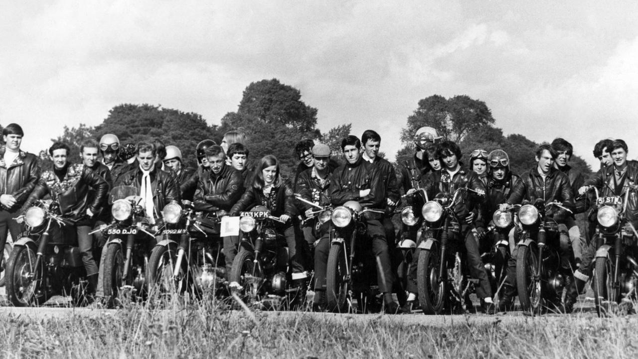 Schwarz-weiß-Foto: Rockergruppe posiert mit Motorrädern auf einer Landpartie in den 1970er Jahren. 