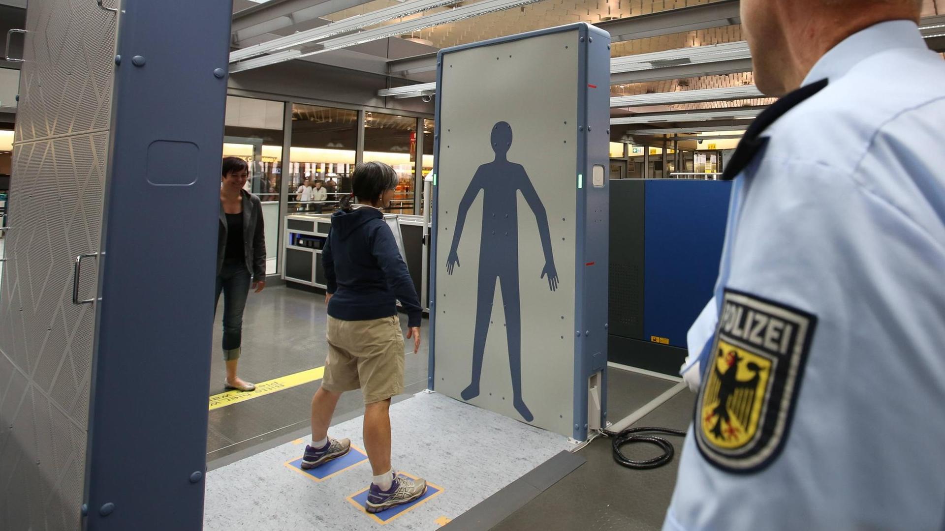 Ein Mann steht am Flughafen vor einer Körperscanner-Wand.