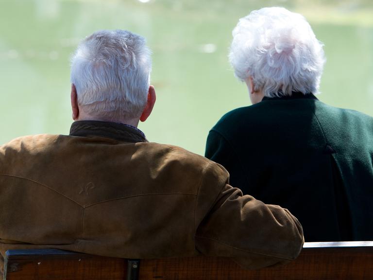 Zwei Senioren sitzen an einem kleinen Teich.