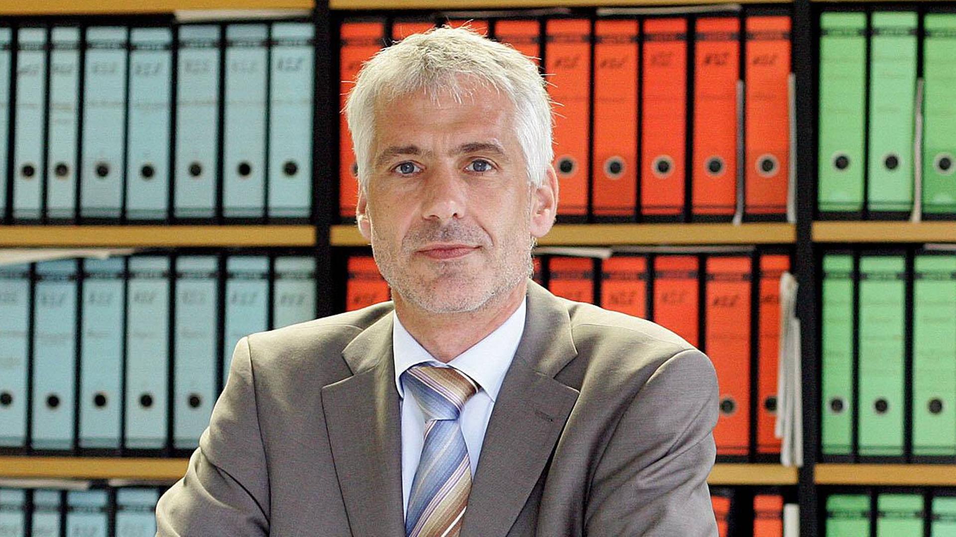 Joachim Ragnitz schaut in die Kamera. Hinter ihm ist ein Bücherregal mit farblich sortierten Aktenordnern. 