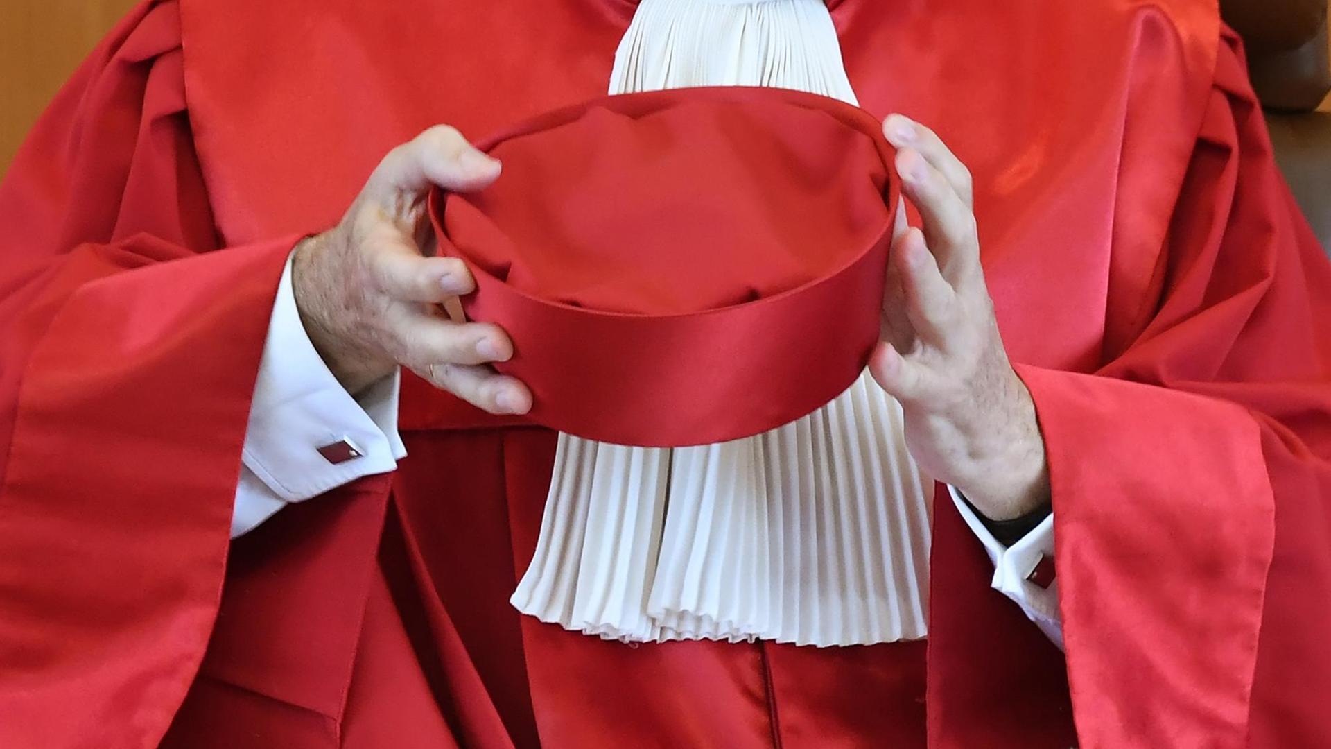 Zu sehen ist ein roter Richterhut in den Armen eines Richters in Robe.
