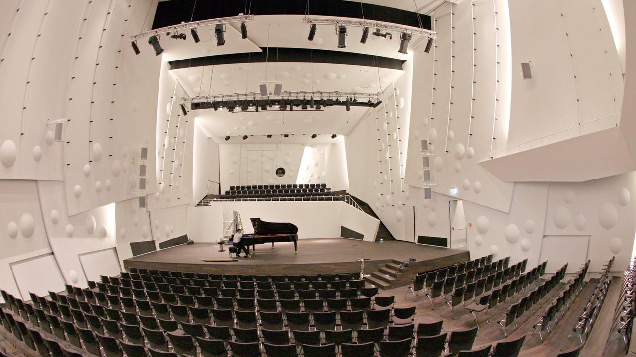 Auf der Bühne im neuen, in Weiß gehaltenen, leeren Konzertsaal der Musikhochschule in Dresden sitzt ein Mann an einem großen Konzertflügel.