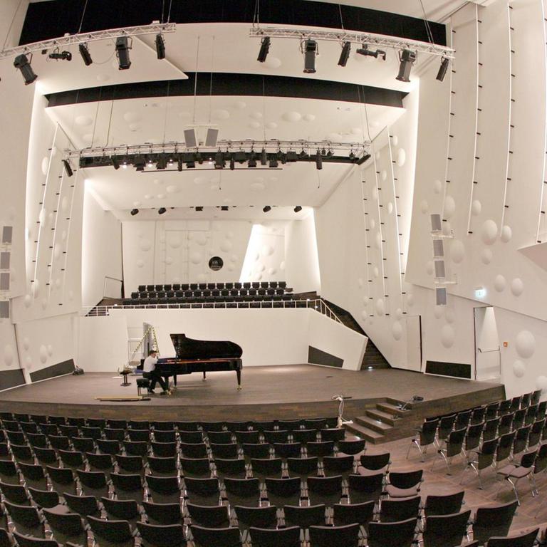 Auf der Bühne im neuen, leeren Konzertsaal der Musikhochschule in Dresden sitzt ein Mann an einem großen Konzertflügel.