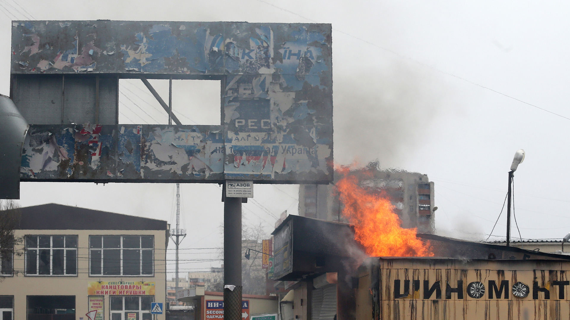 Menschen stehen vor einem brennenden Gebäude in der ostukrainischen Hafenstadt Mariupol.