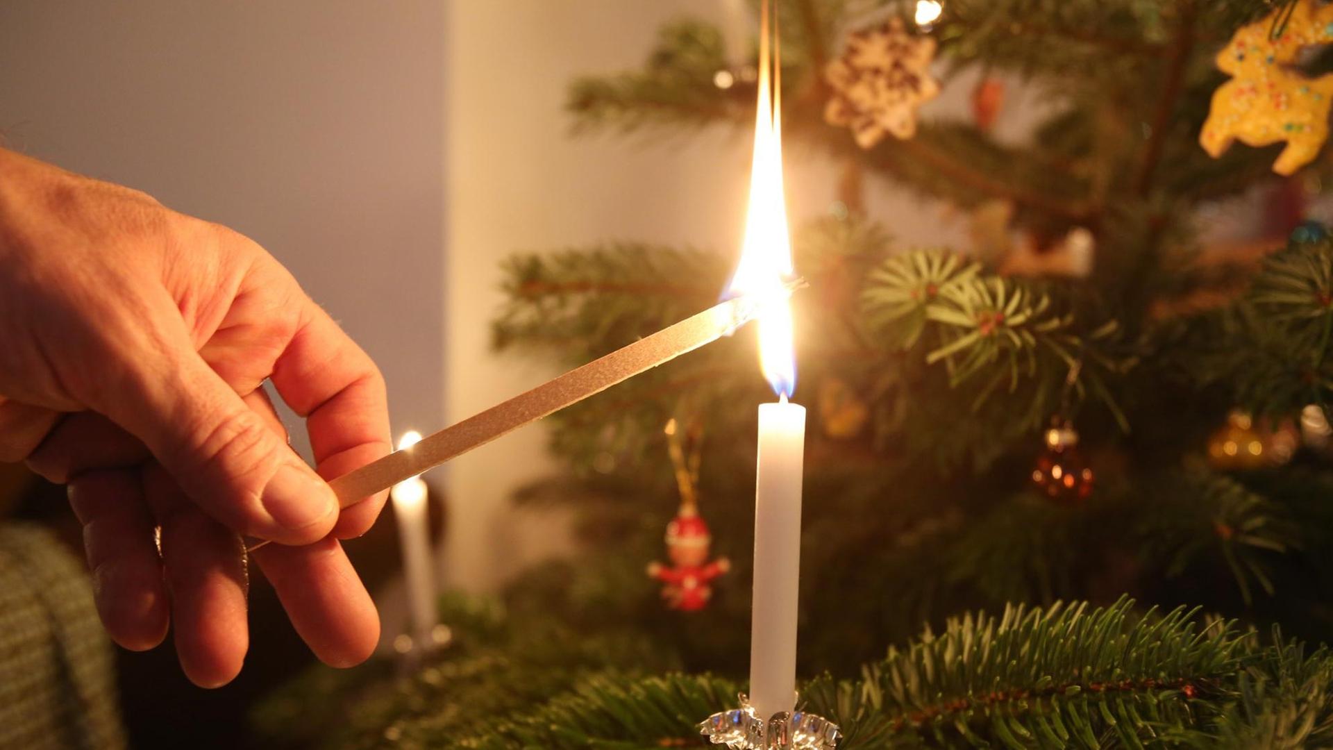 Mit einem großen Streichholz zündet ein Mann eine Kerze an einem Weihnachtsbaum in Hamburg an