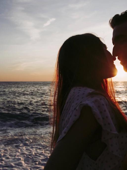 Ein junges Paar küsst sich am Strand bei Sonnenaufgang.