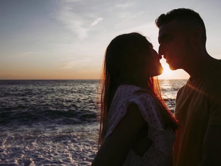 Ein junges Paar küsst sich am Strand bei Sonnenaufgang.