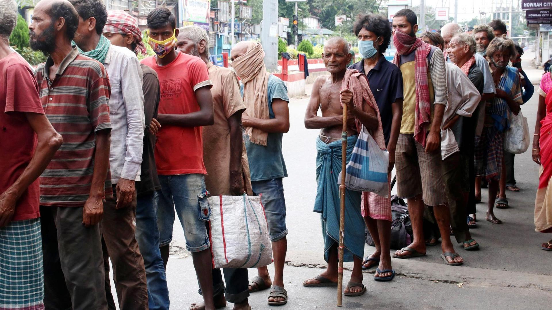 Menschen in ärmlicher Kleidung warten auf eine Essensausgabe in Kalkutta.