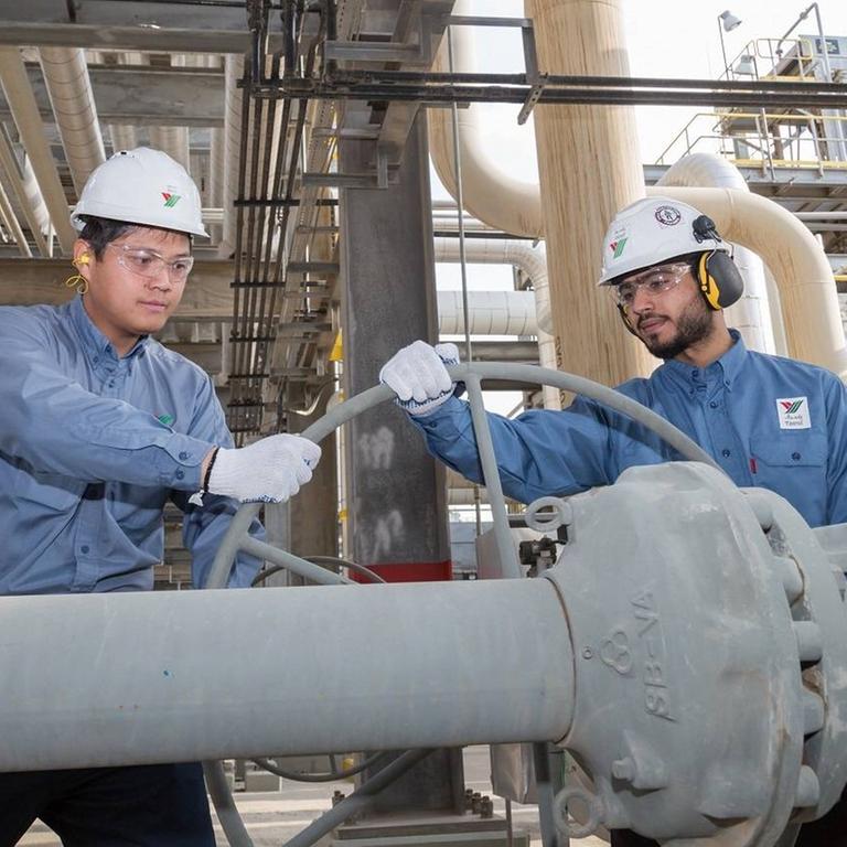 Zwei Arbeiter der saudischen Ölfirma Aramco strehen an einem großen Ventil einer Leitung