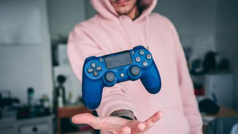 Ein junger Mann mit Kapuzenpulli wirft einen Game Controller in die Luft.