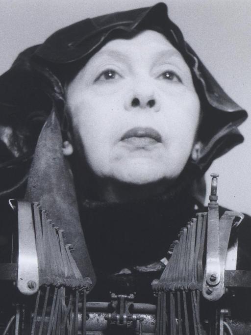 Das Kunstwerk "Mrs Oliver in her traveling costume" von Geta Brătescu. Ein Schwarz-Weiss-Foto das die in ganz in schwarz gekleidete Künstlerin mit einer mechanischen Schreibmaschine zeigt.