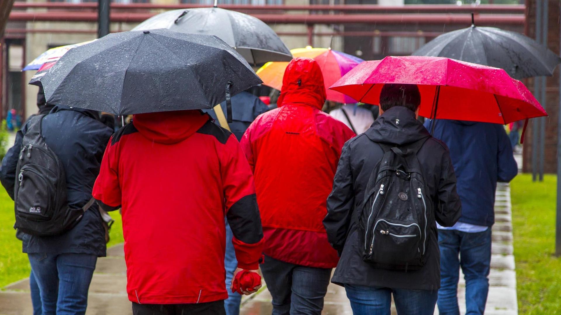 Menschen gehen bei Regenwetter, in Regenkleidung und mit Regenschirmen auf einer Straße
