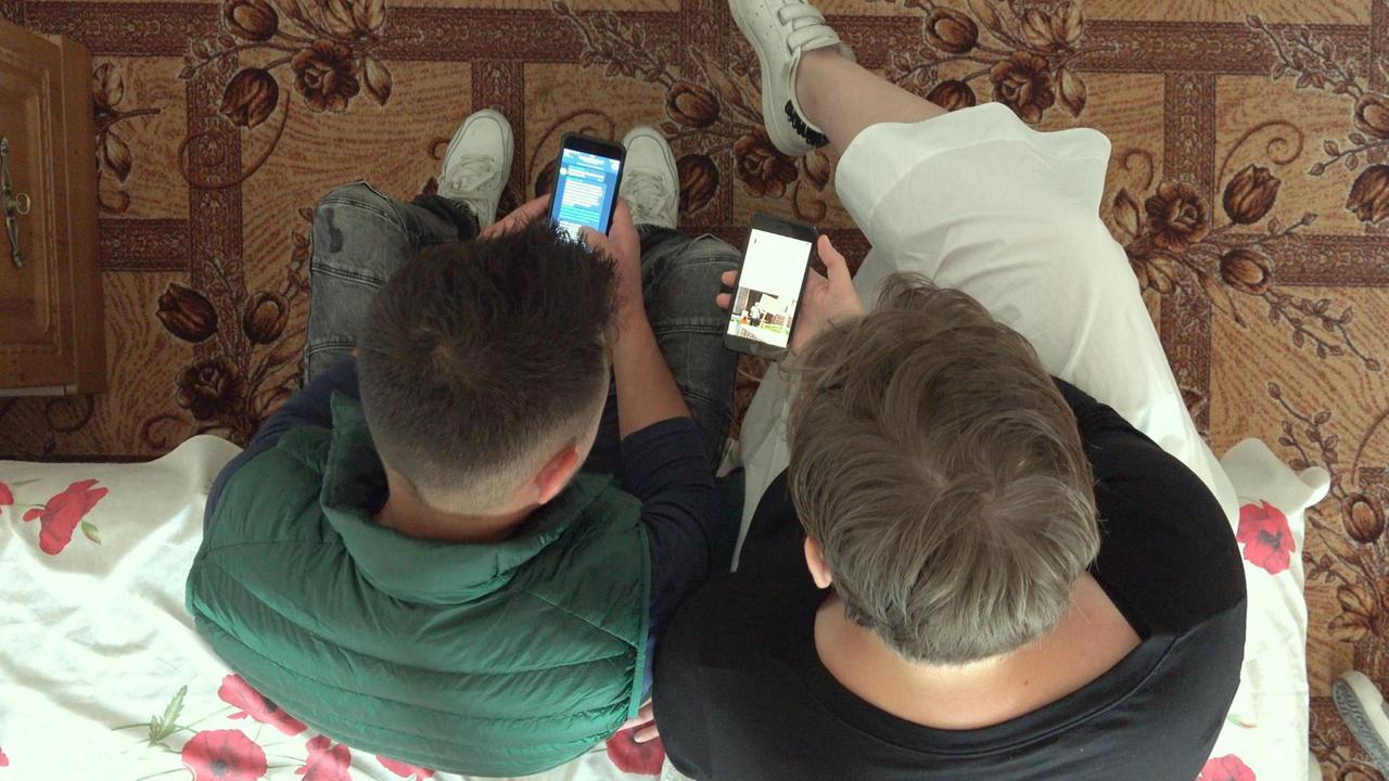 Film-Still aus "Welcome to Chechnya": Zwei Männer sitzen mit Smartphones nebeneinander.
