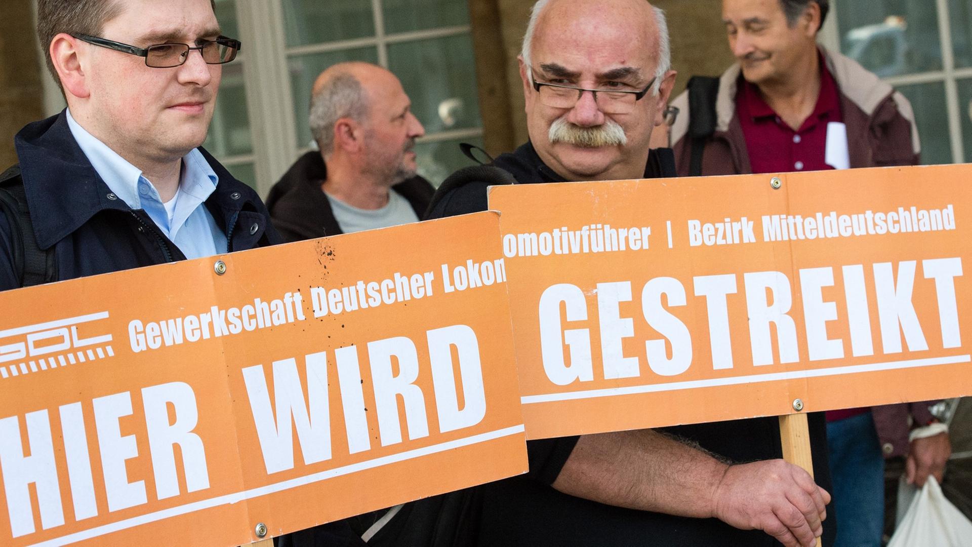 Zwei Lokführer der Deutschen Bahn halten in einem Bahnhof Plakate mit dem Schriftzug "Hier wird gestreikt" vor sich