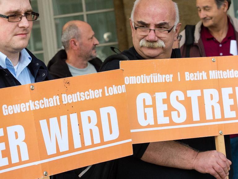 Zwei Lokführer der Deutschen Bahn halten in einem Bahnhof Plakate mit dem Schriftzug "Hier wird gestreikt" vor sich