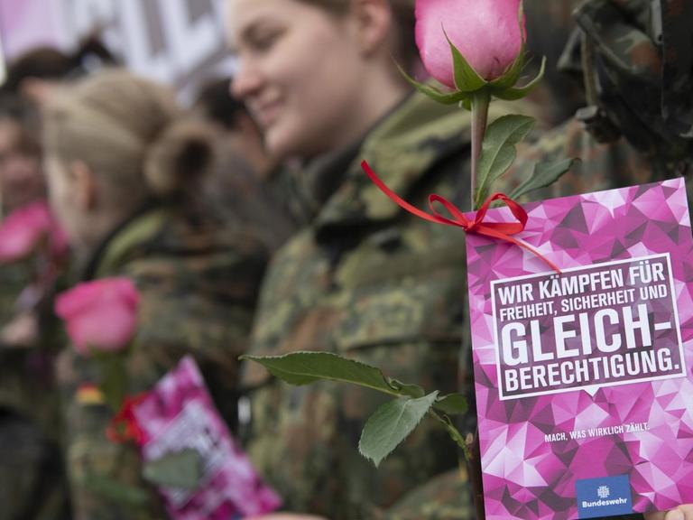 Eine Bundeswehrsoldatin ist schemenhaft hinter einem Flyer zu erkennen, auf dem steht: "Wir kämpfen für Freiheit, Sicherheit und Gleichberechtigung."