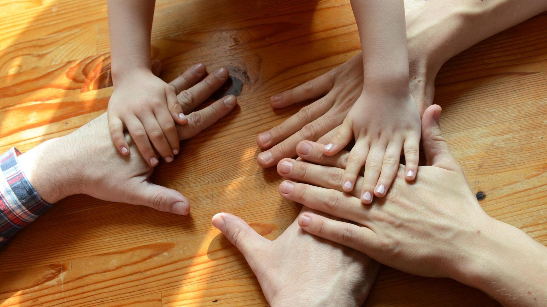 Die Hände eines gleichgeschlechtlichen Paares und eines Kindes liegen auf einem Tisch